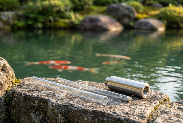 Clear quartz sleeve, a UV-C lamp tube and a stainless steel sterilizer housing on a stone ledge beside a koi pond, used to clear green water and control waterborne pathogens.